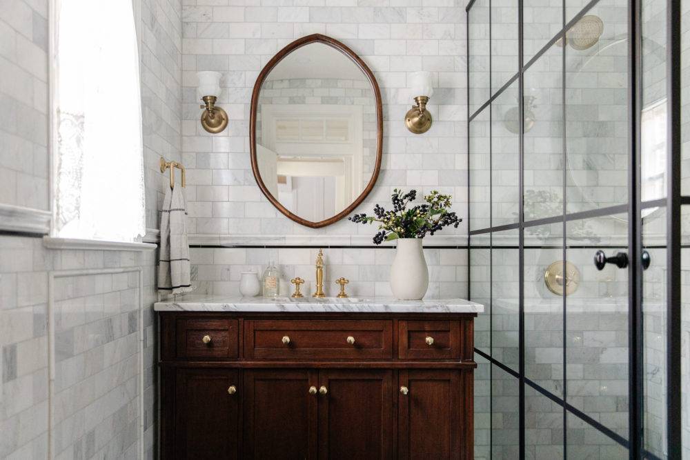 grey marble bathroom with dark cherry wood vanity and oval mirror with glass shower