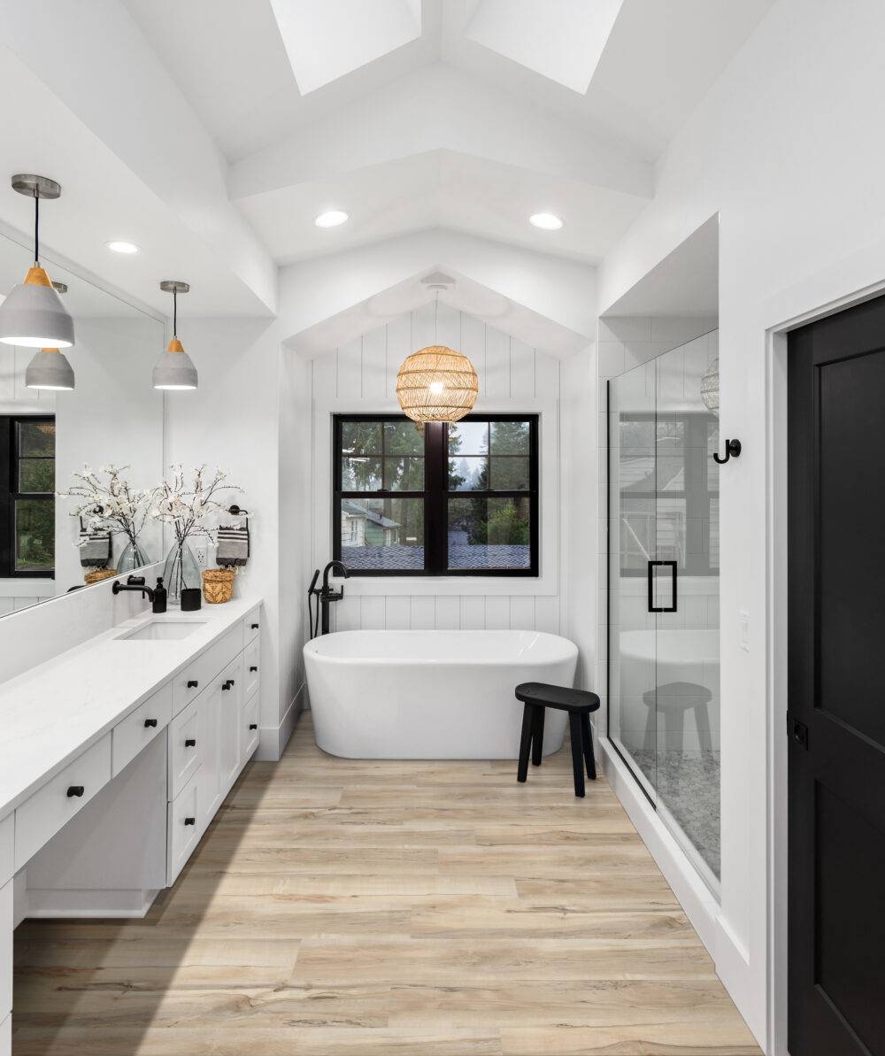 Bathroom in luxury home with double vanity, bathtub, mirror, sinks, shower, and wood-look luxury vinyl floor.