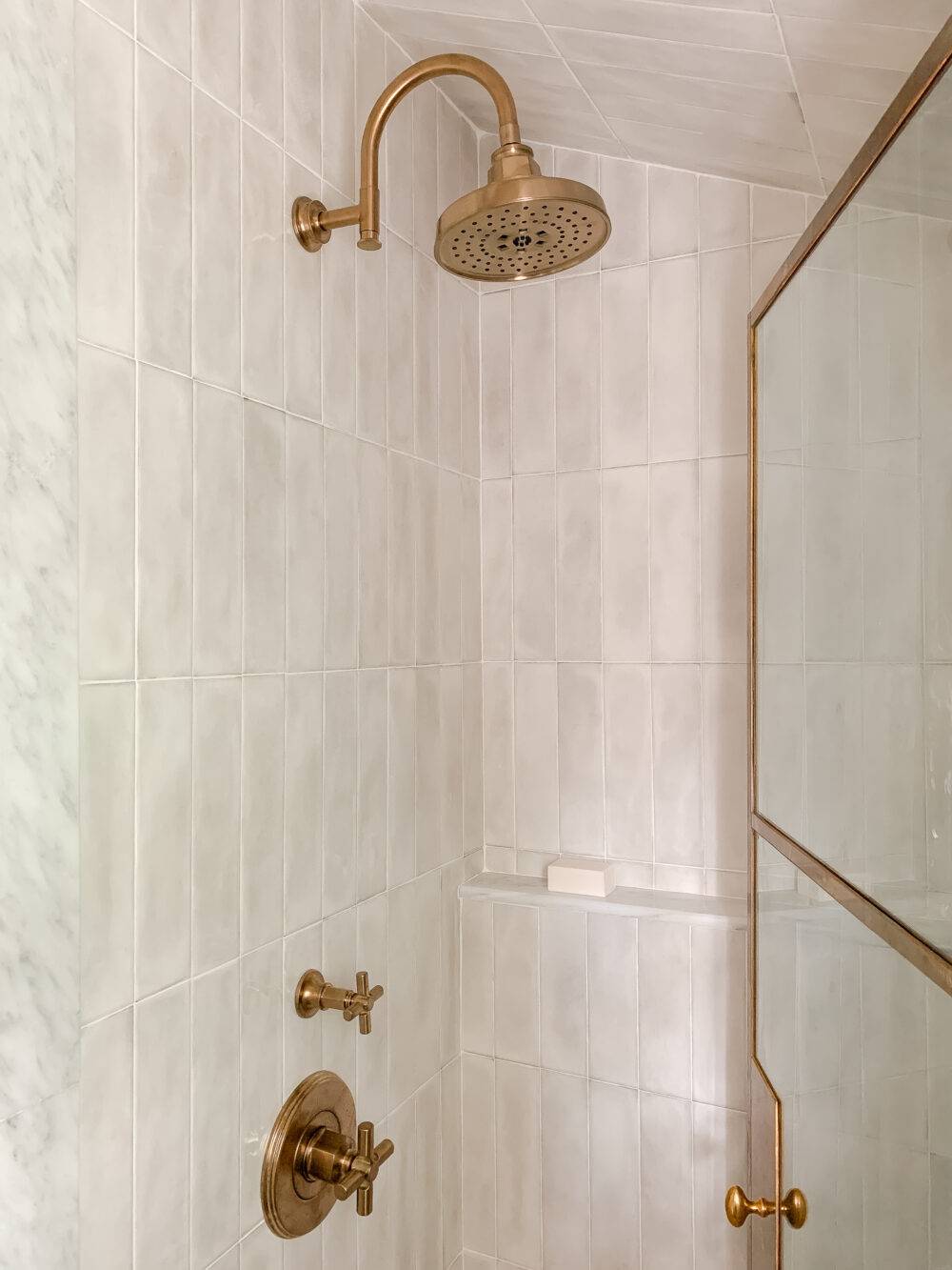 Shower with handmade-look white subway tile and brass fixtures.
