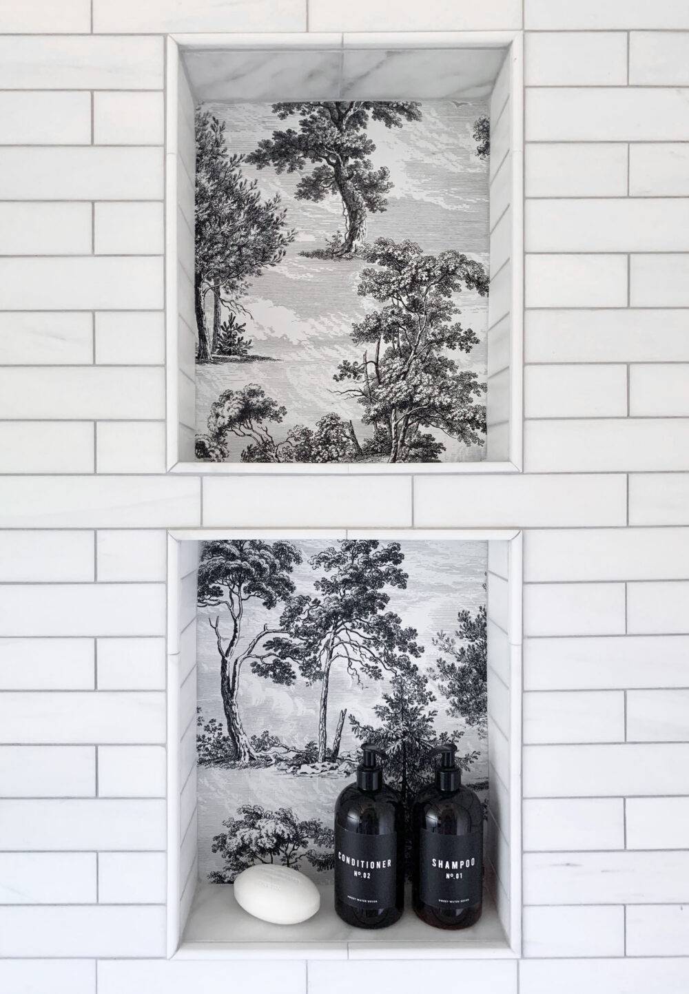 White subway tile shower with black and white tree patterned tile niche. 