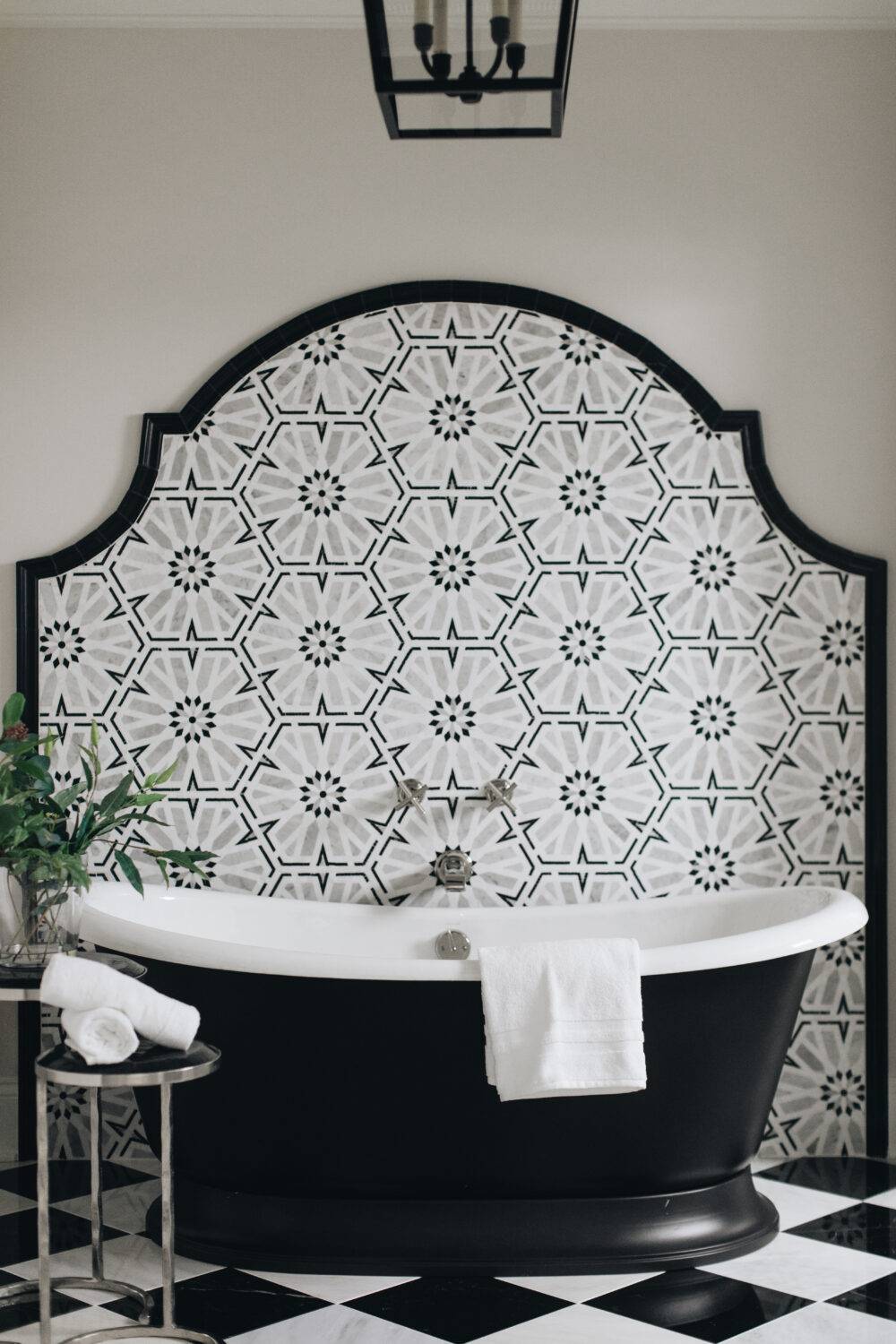 Black, white and grey mosaic tile accent wall with black and white tub and black and white checkerboard marble floor.