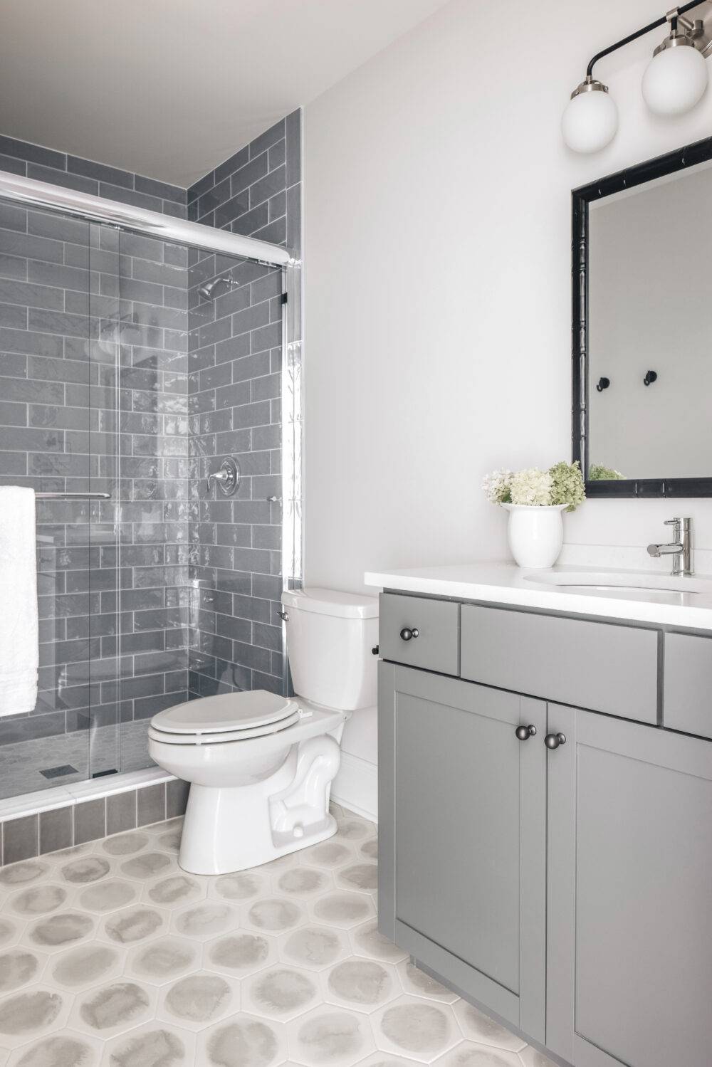 Neutral bathroom featuring Bulevar Grey shower tile and Blot Noon Hexagon floor tile.