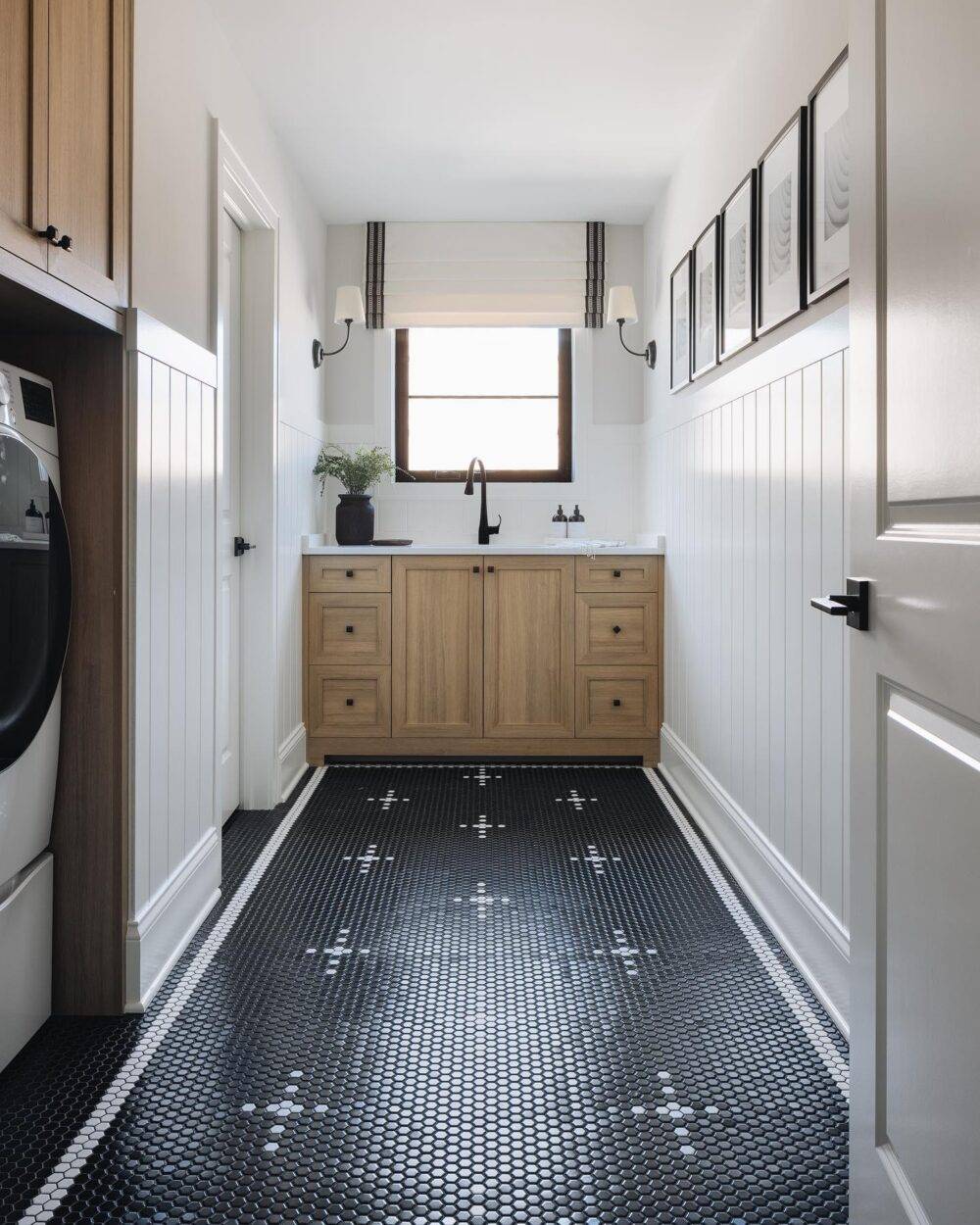 Laundry room with black with a white cross-patterned mosaic floor. Wooden cabinetry.