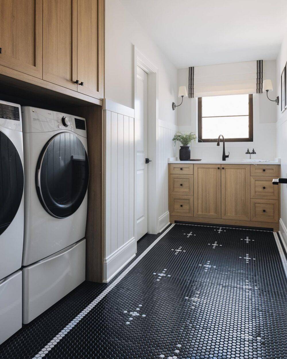 Laundry room with black with a white cross-patterned mosaic floor. Wooden cabinetry.