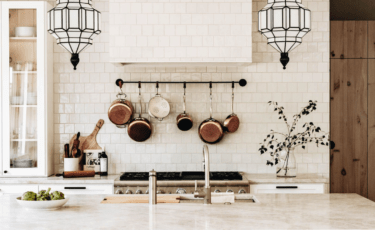 Large kitchen with white square tile backsplash and range hood with hanging pots and pans